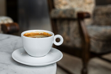 A white cup of black coffee americano in a cozy atmosphere of a cafe with copy space
