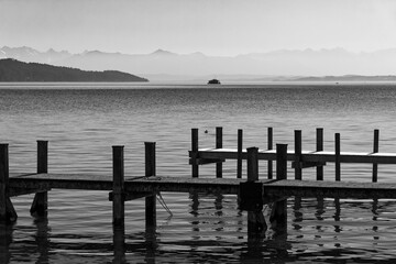 Fototapeta premium Lake called Ammersee with a wooden landing pier and the bavarian mountains in the background, black and white photo, Alps, Bavaria, Germany, Europe