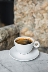 A white cup of black coffee americano in a cozy atmosphere of a cafe with copy space
