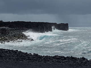 Pahoa, Hawaii Island, Hawaii, USA - July 15, 2025: Pohoiki Black Sand Beach landscape with white surf  crashing ocean waves under heavy dark gray cloudscape
