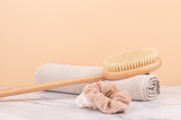 Wooden body brush, beige towel and fabric scrunchies on marble table with peach background. Horizontal image with copy space inspired by natural self care routine. Concept of slow beauty and wellness