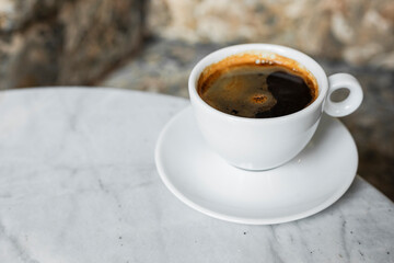 A white cup of black coffee americano in a cozy atmosphere of a cafe with copy space
