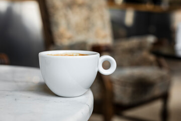 A white cup of black coffee americano in a cozy atmosphere of a cafe with copy space
