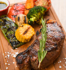 Grilled beef steak with rosemary on a wooden board, served with roasted zucchini and peppers.