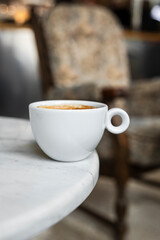 A white cup of black coffee americano in a cozy atmosphere of a cafe with copy space
