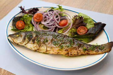 Grilled seabass with salad and onion on a white plate