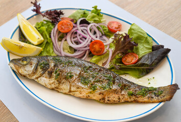 Grilled seabass with salad and onion on a white plate