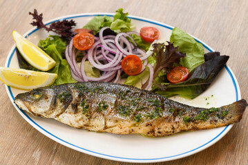 Grilled seabass with salad and onion on a white plate