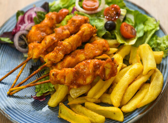 Chicken kebab on skewers with french fries and salad.