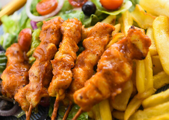 Chicken kebab on skewers with french fries and salad.