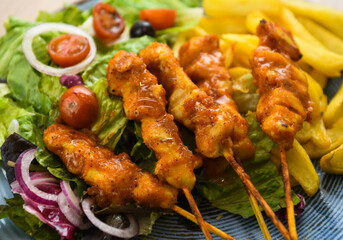 Chicken kebab on skewers with french fries and salad.