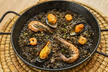 Paella with black rice, mussels and shrimps in a pan