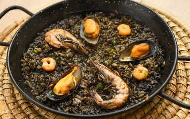 Paella with black rice, mussels and shrimps in a pan