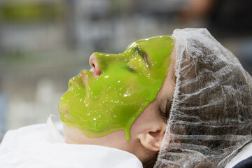 Side View of Woman Receiving Bright Green Alginate Facial Mask in a Spa