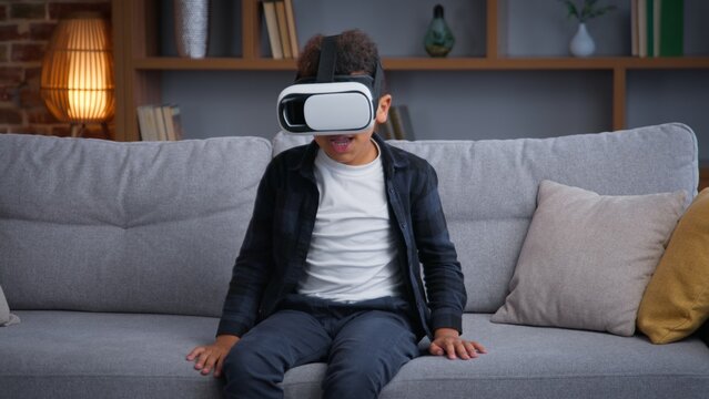 African American child boy kid son playing VR game at home play online 3d gaming with virtual reality glasses augmented headset AR technology gaming playing metaverse pretending fighting innovation