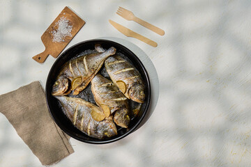 Grilled dorado fish served with lemon slices and garnished with salt on a rustic wooden table.
