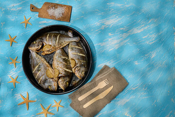 Freshly cooked dorado with lemon slices served on a rustic table with sea stars and coarse salt