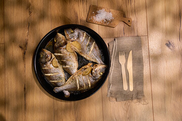 Grilled dorado fish served with slices of lemon and sea salt on a dark plate with a rustic setting