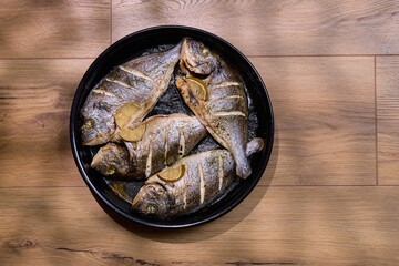 Grilled dorado fish served with slices of lemon and sea salt on a dark plate with a rustic setting