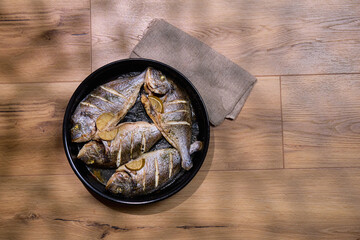 Grilled dorado fish served with slices of lemon and sea salt on a dark plate with a rustic setting