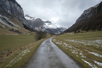 Fototapeta premium Scenic mountain road winding through snow-capped peaks and green fields in early spring
