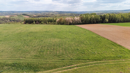 Aerial view of green fields and patches of farmland under a partly cloudy sky. This tranquil landscape showcases the beauty of rural scenery during springtime.
