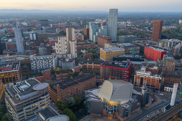 Aerial view of Manchester cityscape with modern high-rises, red buildings, and early daylight atmosphere.
