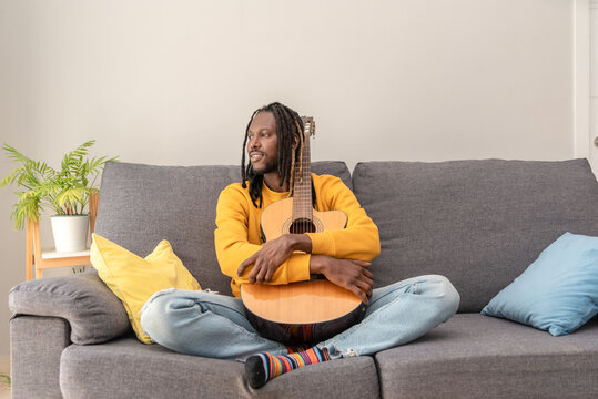 African american man embracing acoustic guitar sitting on sofa enjoying a peaceful moment at home
