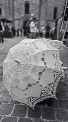 Black white photo of one open white lace parasol on the pavement, on the street market. Selective focus.