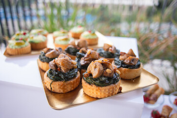 Appetizing tarts with stewed mushrooms and spinach in close-up on a golden tray, served outdoors.