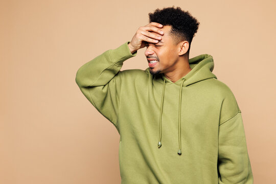 Young sad man of African American ethnicity wear green hoodie casual clothes put hand on face facepalm mistaken omg gesture isolated on plain pastel light beige background Lifestyle concept