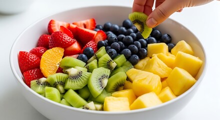 Fresh Fruit Salad Bowl with Hand Adding Kiwi Slice.
