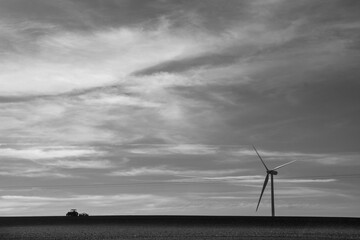 le paysage rural de demain: une tracteur en train de labourer un champ au milieu duquel se trouve une éolienne produisant de l'énergie verte durable