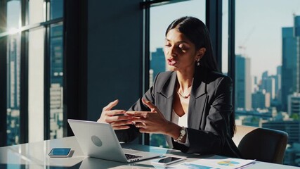 A professional woman in a suit works on a laptop in a modern office. The side angle captures her focus, perfect for a business video setting.