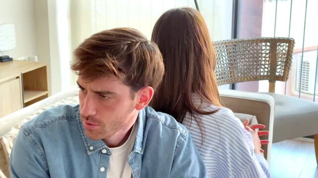 Serious couple sitting on sofa at home talking and confronting each other, thoughtful and sad mood as if during relationship therapy or difficult conversation, concept of communication, crisis and emo