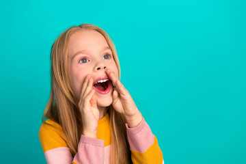 Charming young girl enthusiastically calling out with hands cupped, wearing stylish striped sweater against teal background