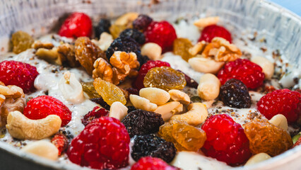 A vibrant and healthy yogurt bowl topped with fresh raspberries, a mix of nuts and dried fruits, chia and pumpkin seeds. A delicious and nutritious breakfast or snack.