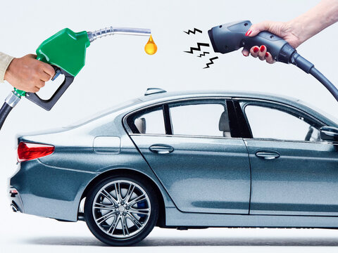 Concept between classic car petrol fuel and electric vehicle with hands holding gas fuel pump and electric charger