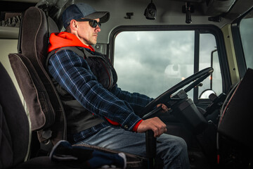 Obraz premium Experienced Trucker Driver Focused on the Road in a Heavy Truck During Cloudy Weather