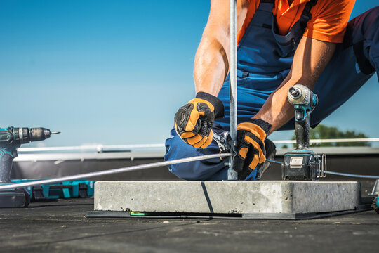 Worker Installing a Metal Lightning Protection Rod on a Roof During a Clear Sunny Day