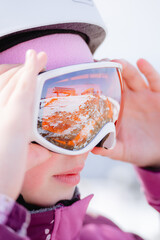 A close-up portrait of a girl putting ski goggles on her face