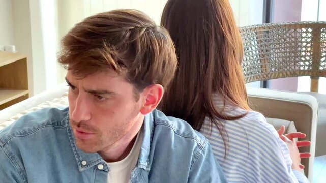 Serious couple sitting on sofa at home talking and confronting each other, thoughtful and sad mood as if during relationship therapy or difficult conversation, concept of communication, crisis and emo