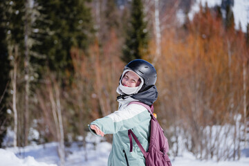 A positive girl with a backpack and a helmet on her head among mountain forests