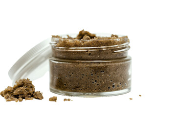 Natural exfoliating scrub in a clear jar with textured powder spilling out on a white background