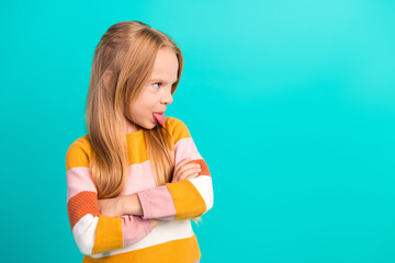 Adorable young girl expressing playful emotions against a turquoise background wearing a colorful striped sweater © deagreez