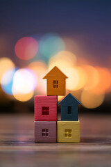 Colorful toy houses stacked, symbolizing home ownership, real estate, and property investment against blurred city lights.
