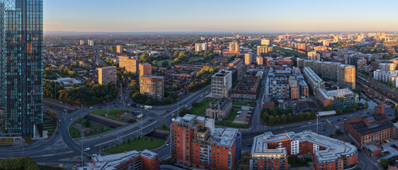 Aerial sunrise view over Manchester featuring Deansgate Square, Mancunian Way roundabout, and Chester Road leading toward Old Trafford.