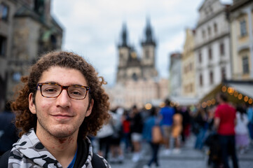 Fototapeta premium Prague, Czech Republic, August 7, 2023. Portrait of a young Caucasian man looking into the camera in the iconic and crowded Old Town Square. Blurred background, travel destinations.