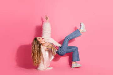 Young woman posing in trendy outfit against pink backdrop with dynamic gesture, showcasing fun