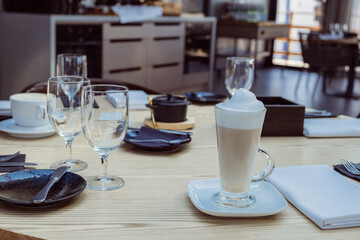 Coffee beverage served in a tall glass on a wooden table, surrounded by elegant tableware and glassware, creating a cozy dining atmosphere with inviting ambiance